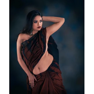 Desi model in rust and black sari with striking blue eyes and burgundy lips against moody blue-gray gradient background with dramatic lighting