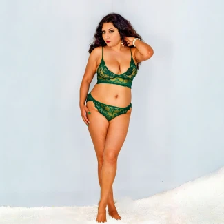 Sumana Sengupta in emerald green lace lingerie set with floral motifs and deep red lipstick posing confidently against light blue background on fluffy white rug