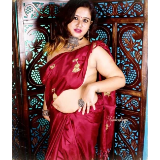 Desi woman with exposed left breast and gold jewelry poses confidently in a red braless saree