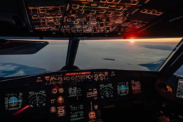 Inside an airplane cockpit, bathed in the warm glow of sunset, showcasing the instrument panel and the horizon.