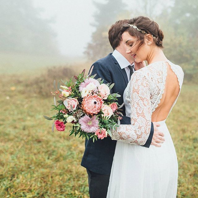 A bride and groom embrace, holding a bouquet in a dreamy, romantic outdoor wedding scene.