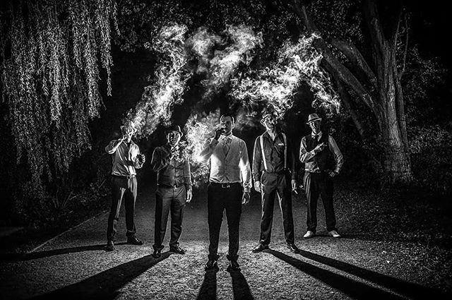Five men in suits dramatically smoke cigars at night, creating a vintage and mysterious atmosphere.