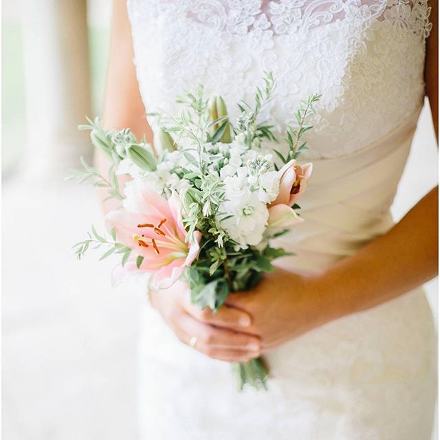 A bride in a lace dress holds a delicate bouquet of pink and white flowers.