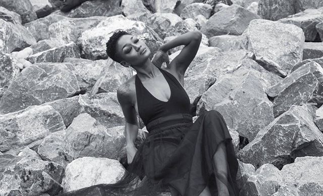 A woman in a dress poses gracefully among rocks, captured in a serene monochrome image perfect for editorial use.