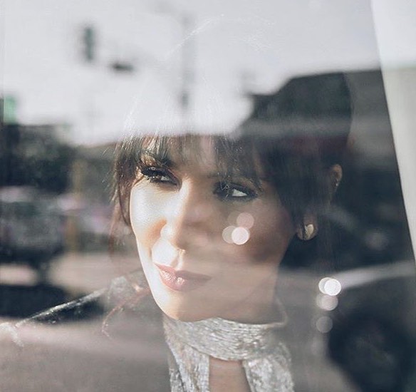 A brunette woman gazes dreamily through a window, showcasing elegance and natural beauty.