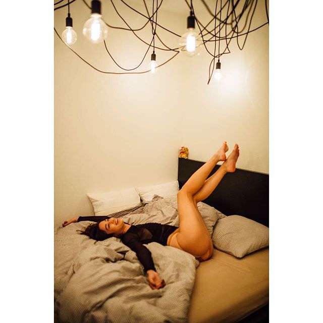 A woman relaxes on a bed in a softly lit bedroom, enjoying a moment of calm.