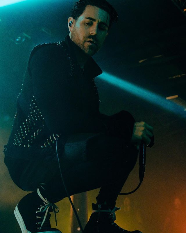 A man crouches holding a microphone during a concert performance.
