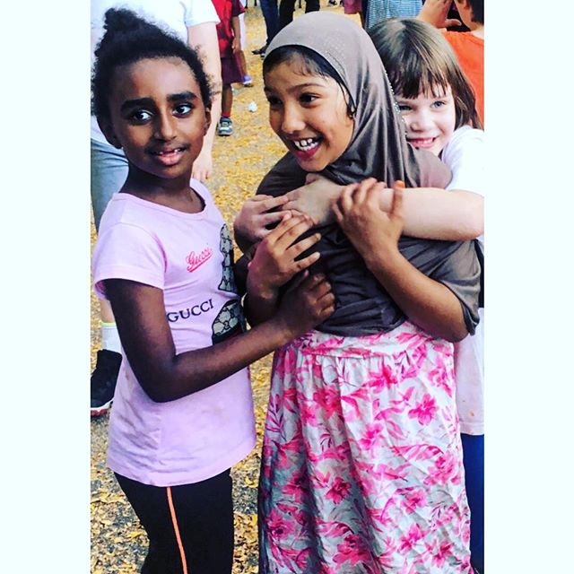 Three young girls embrace, smiling and enjoying a day outdoors in a heartwarming display of friendship and cultural diversity.