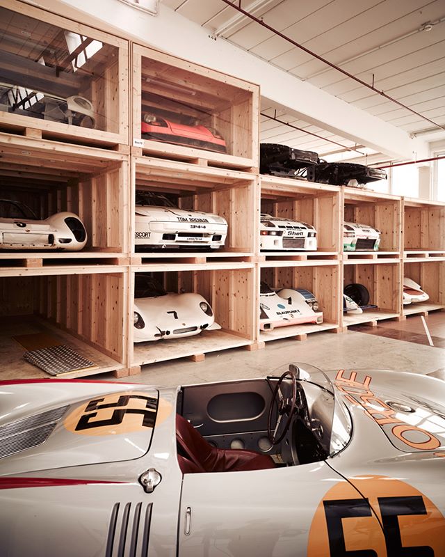 A collection of classic race cars stored in wooden crates inside a warehouse.