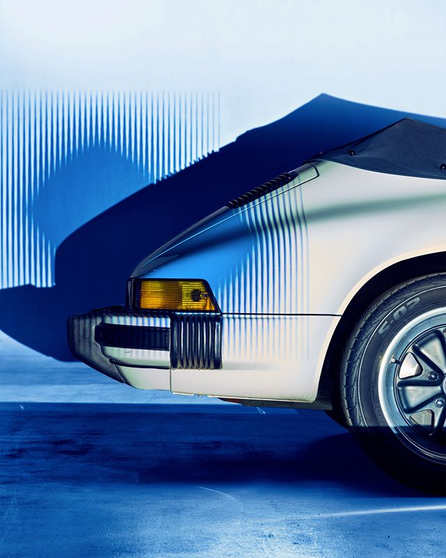 A close-up of a vintage car's front in a blue-lit studio setting, highlighting its design and classic appeal.
