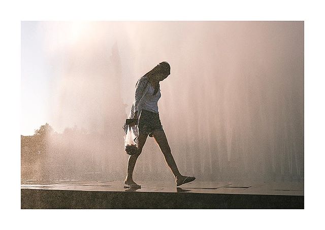 A woman walks through a misting fountain in an urban setting, creating a serene and refreshing moment.