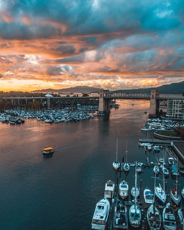 Scenic aerial view of a marina with boats, a bridge, and mountains under a colorful sky at dusk.