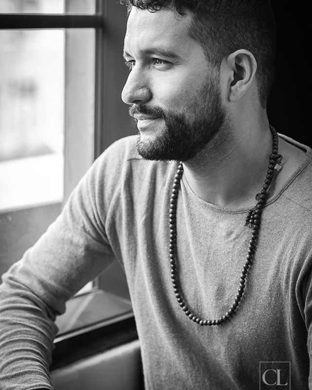 A man with a beard gazes out the window in a thoughtful, black and white portrait.