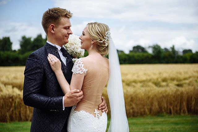 A bride and groom embrace in a field on their wedding day, sharing a tender moment.