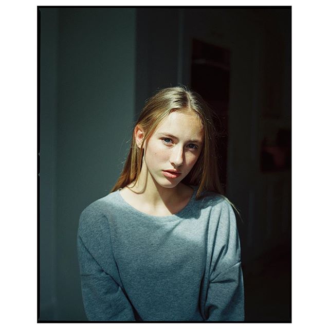 A young woman with blonde hair poses in soft window light for a simple, natural portrait.