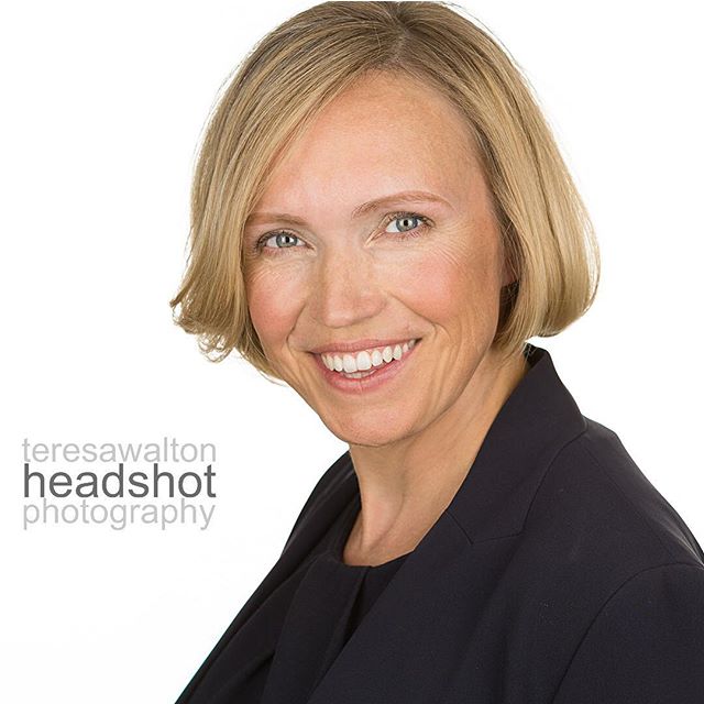 A smiling woman in a dark blazer is professionally posed in a studio headshot.