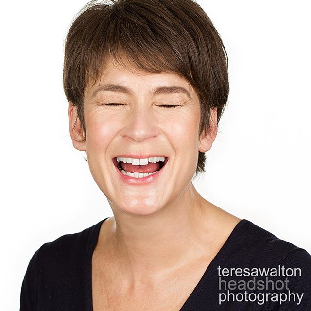 A cheerful woman laughs with her eyes closed in a bright, professional headshot on a white background.