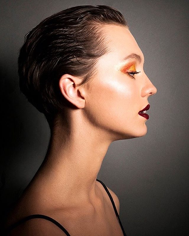 A woman with bold makeup and slicked-back hair poses in a beauty portrait.