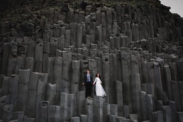 A bride and groom pose in front of a basalt column rock formation in Iceland.