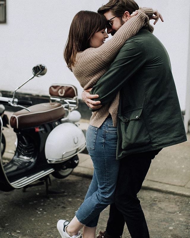 A young couple embraces by a motor scooter in an urban setting, radiating love and affection.
