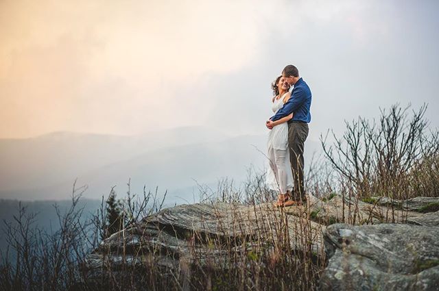 A couple embraces lovingly on a mountain top, enjoying the scenic view.