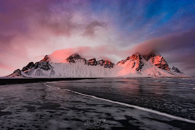 Snow-covered mountains meet the sea under a colorful sky, creating a scenic landscape in Iceland.
