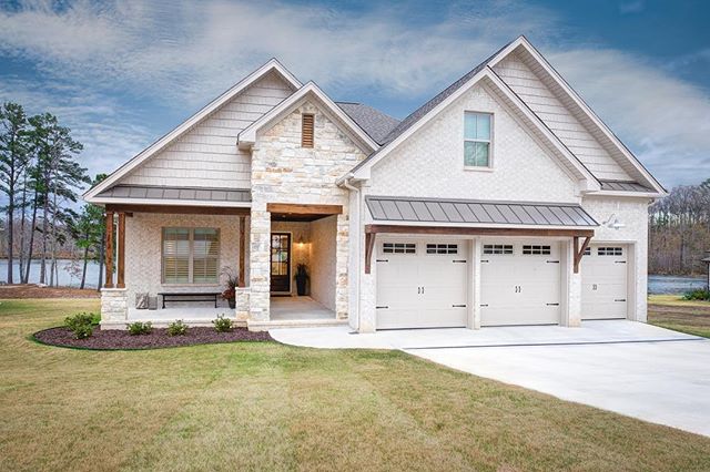 A modern craftsman-style house exterior with white brick, stone accents, and a well-maintained lawn and driveway.