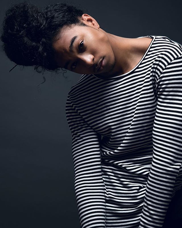 Portrait of a stylish man in a black and white striped shirt, posing in a studio setting.