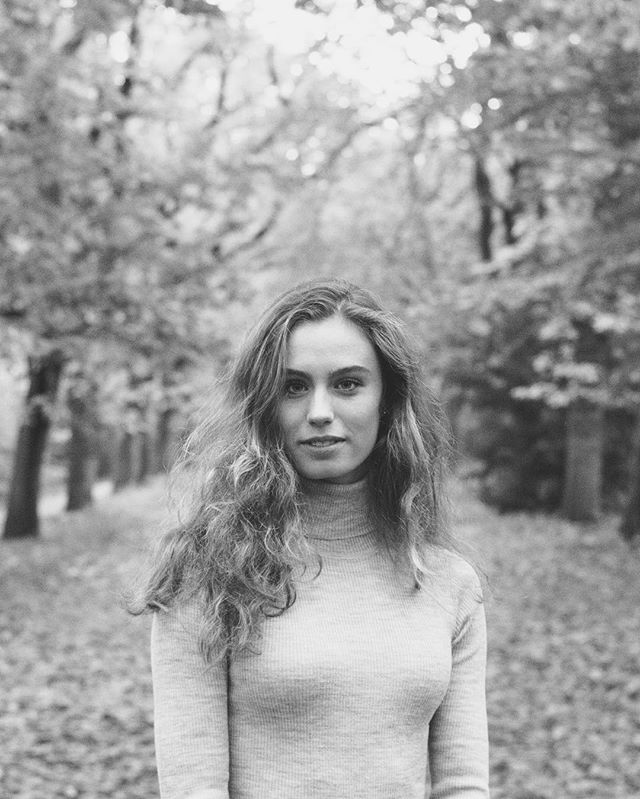 A young woman with long hair poses naturally outdoors in a black and white portrait, exuding serene vibes.