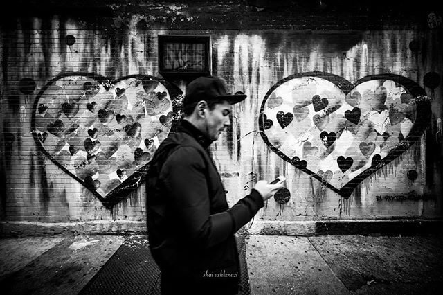 A man walks by a brick wall with heart graffiti in black and white, creating an urban street scene.