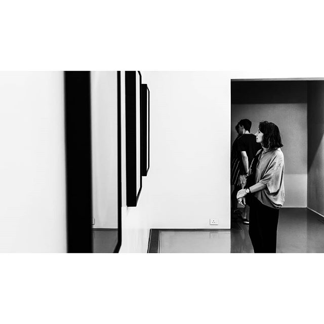 A woman and a man admiring art in a modern, minimalist gallery, captured in a striking black and white composition.