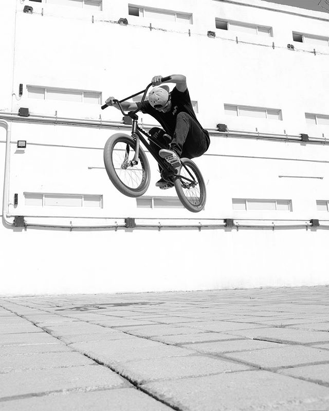 A bmx rider in mid-air performs a trick in an urban setting, captured in dynamic black and white.