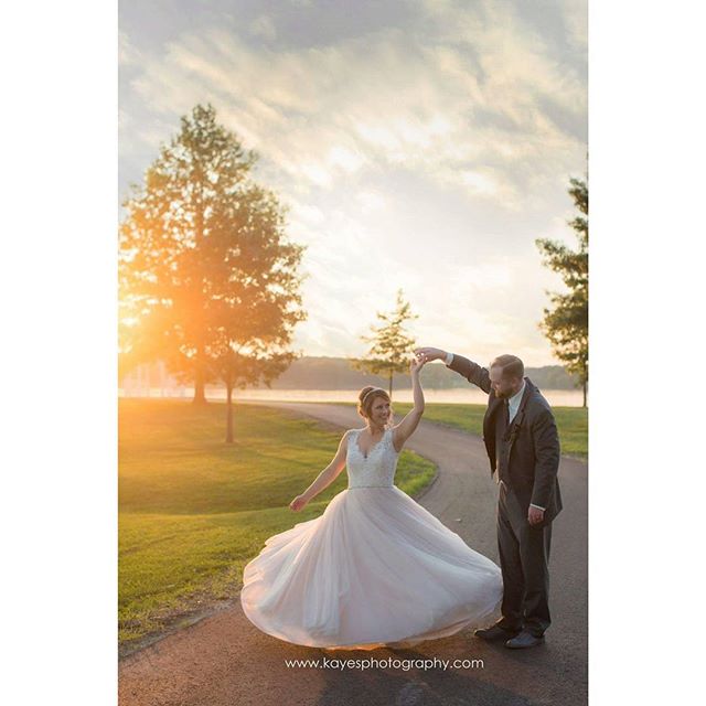 A bride and groom share a tender moment dancing on their wedding day in a picturesque park setting during golden hour.