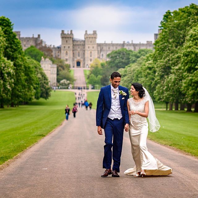 A bride and groom walk hand-in-hand on a path leading to a castle on their wedding day.