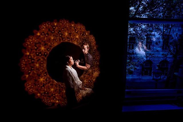 A woman gets her makeup done inside, reflected in a window with a night view outside.