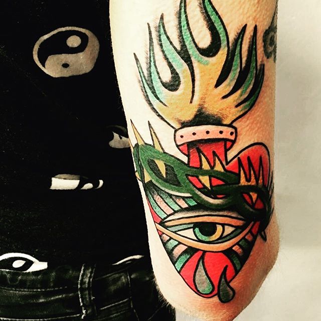 A vibrant, colorful tattoo design featuring a heart, eye, and flame on an arm.