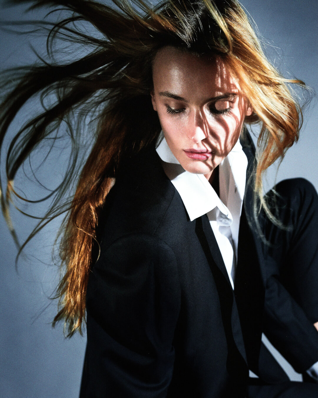A woman in a blazer poses in a studio, illuminated by soft, side lighting for an editorial fashion shot.
