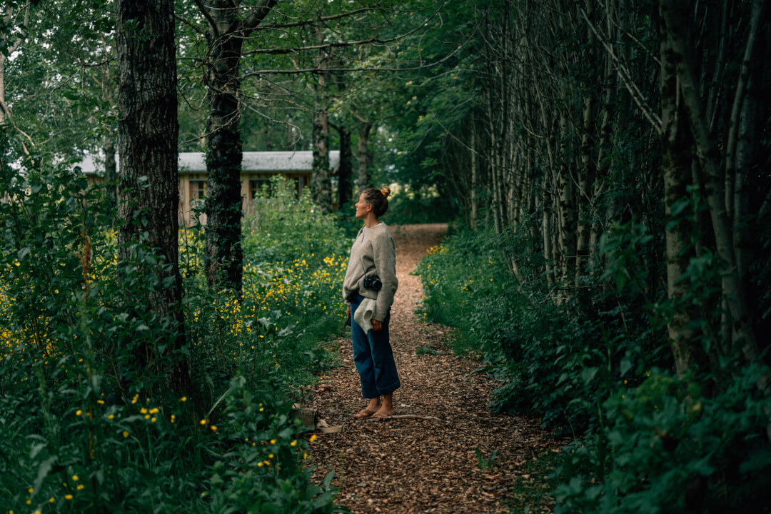A woman walks barefoot on a path in a serene forest setting.