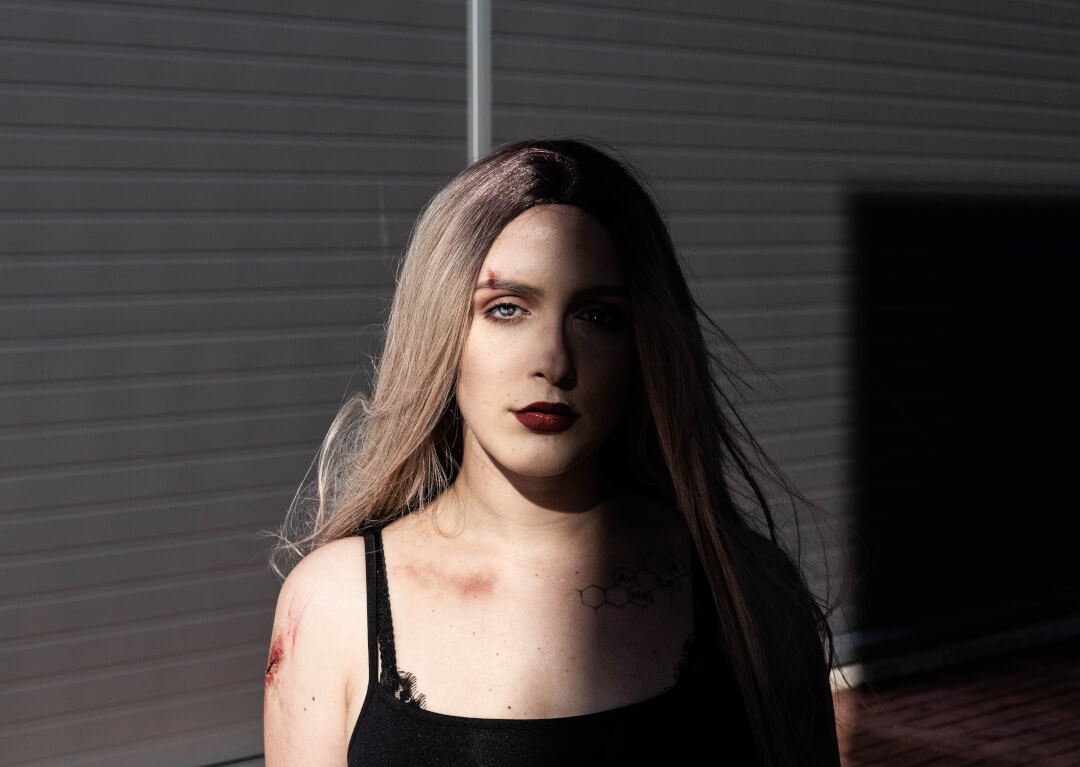 A portrait of a young woman with striking blue eyes and dramatic makeup under harsh sunlight.