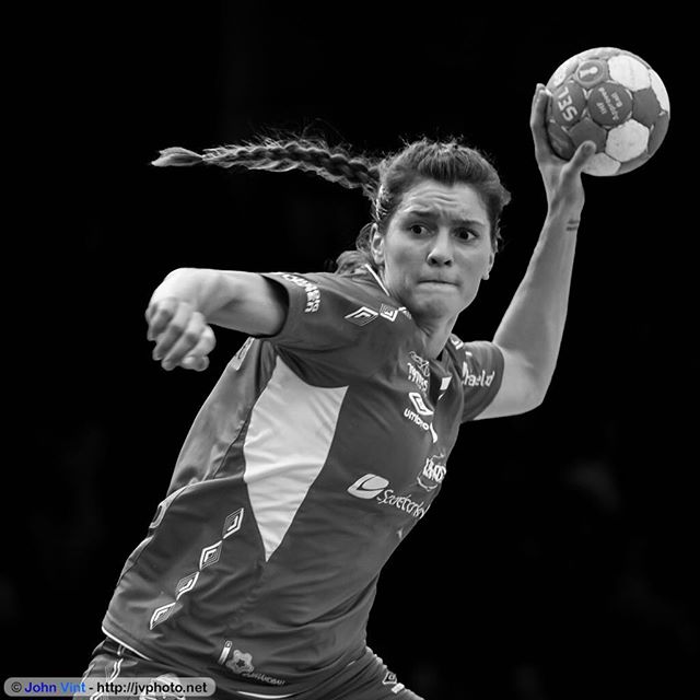 A female handball player in action, captured in a black and white medium shot.