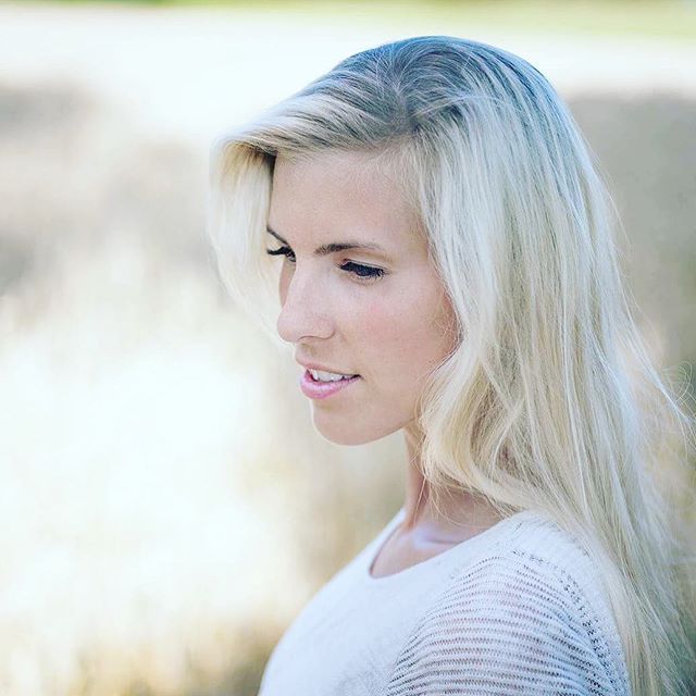 A serene woman with blonde hair poses outdoors in soft lighting for a natural portrait.