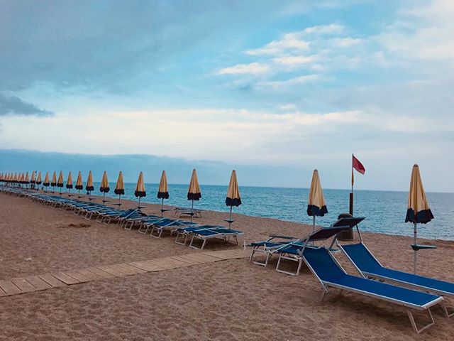 A tranquil beach with a row of umbrellas and deck chairs under a cloudy sky. Perfect for a relaxing summer getaway.