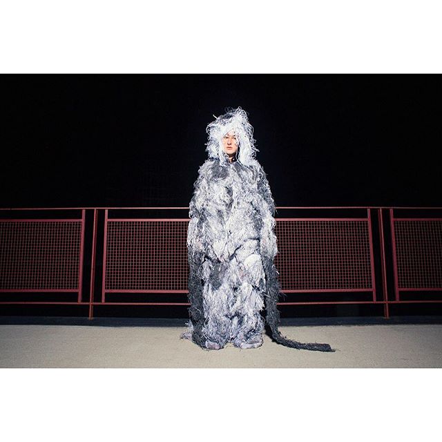 A person in a textured gray and white costume stands outdoors, a unique and artistic display of creative expression.