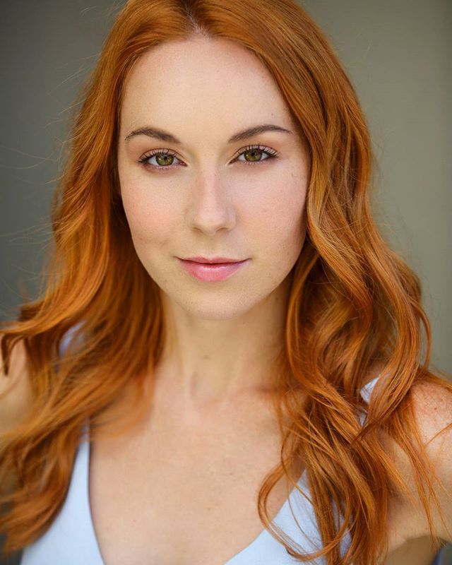 Portrait of a redhead woman with fair skin and hazel eyes in a light blue top.
