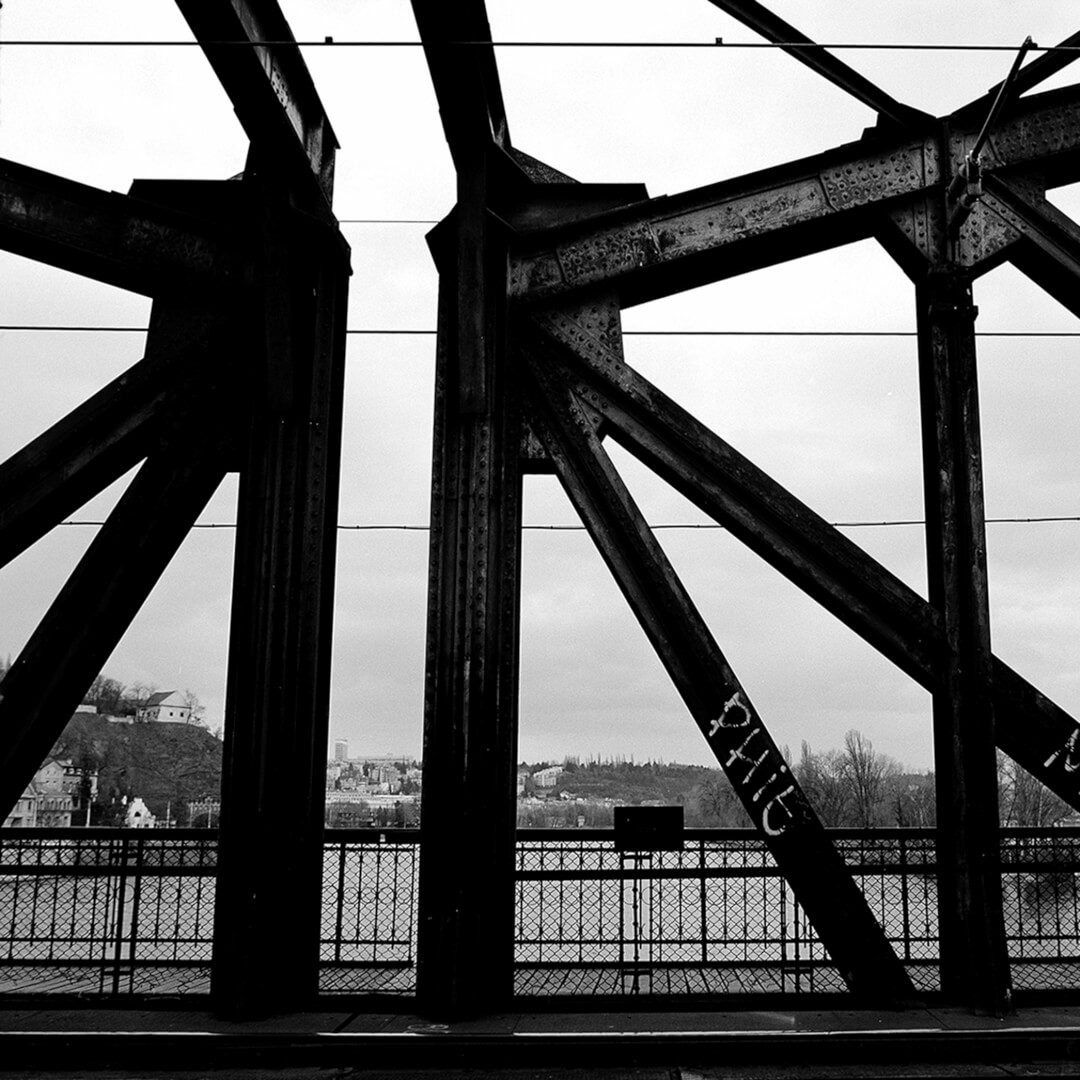 A black and white image of a steel bridge featuring industrial architecture and graffiti.