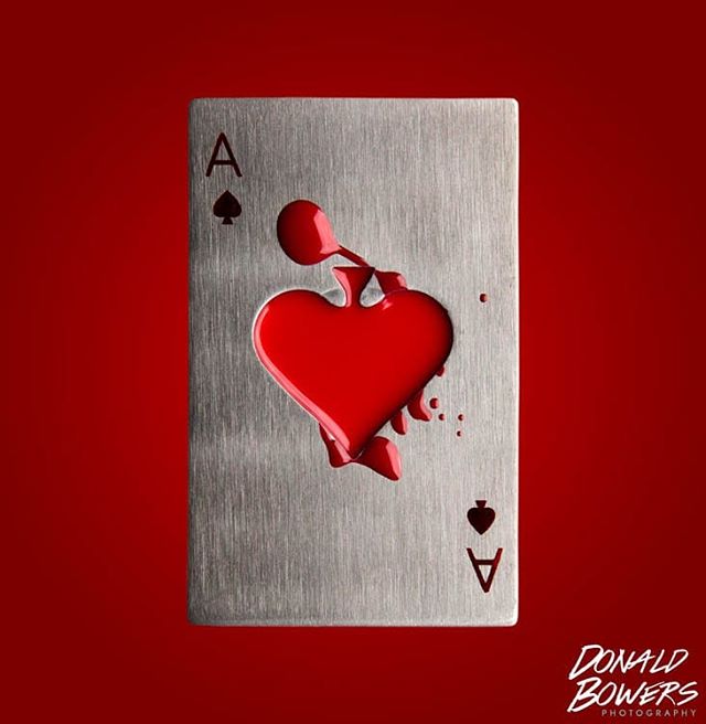 An ace of spades playing card with a heart shape filled with dripping red paint on a red background.