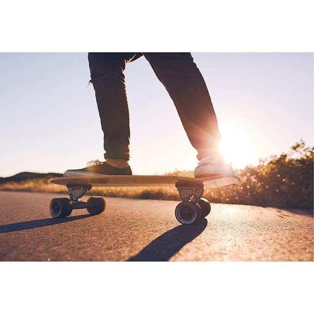 A person is riding a skateboard on a road during sunset, conveying an active lifestyle.