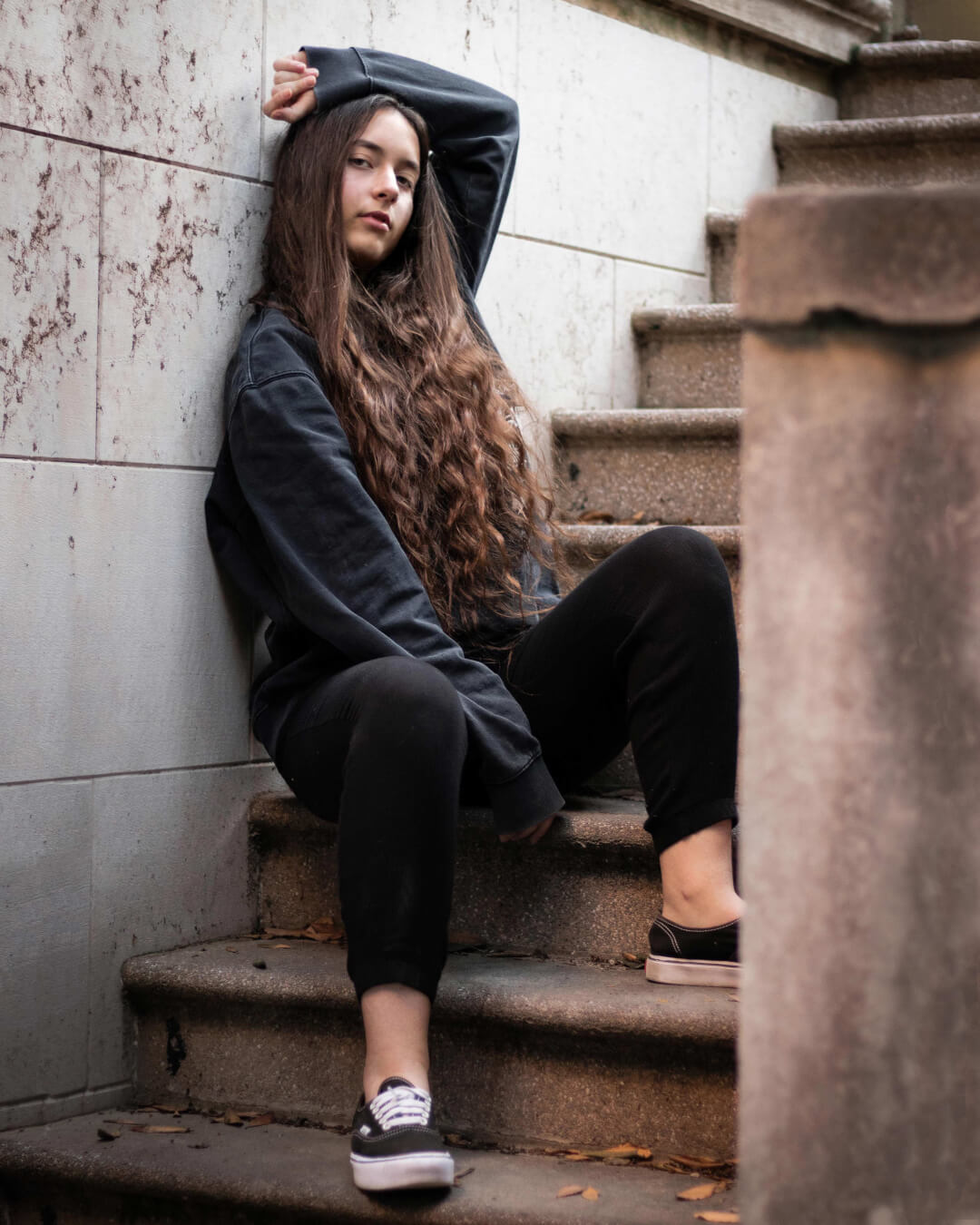 A young woman sits on stone stairs, posing in a casual outfit for a candid urban portrait.