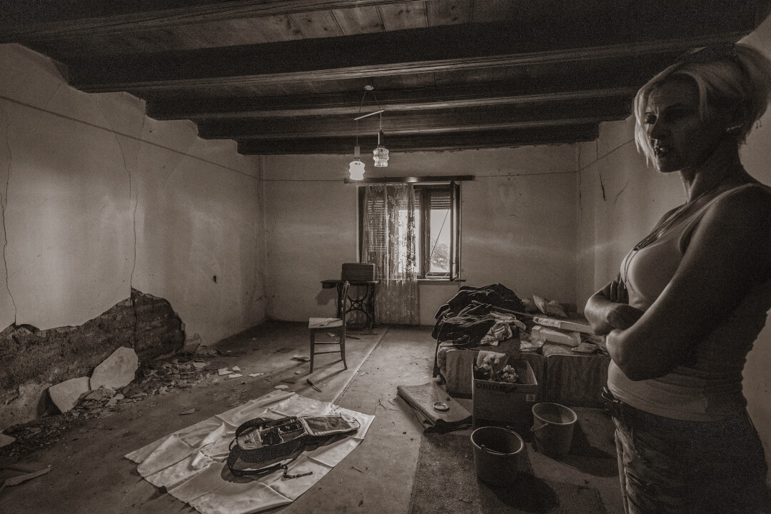 A woman stands in an abandoned room with peeling paint and debris, creating a moody and intense atmosphere.
