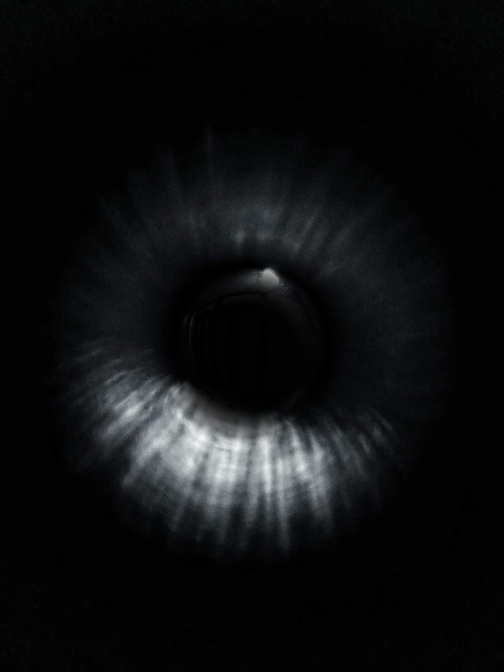 An abstract, monochrome close-up of an eye, focusing on the iris and pupil against a dark background.